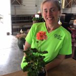 woman with green shirt at counter with geranium plant