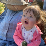 little girl with look of excited wonder sitting with scarecrow on hay bale