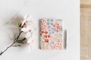 a journal with a floral cover, a pen, and some white flowers